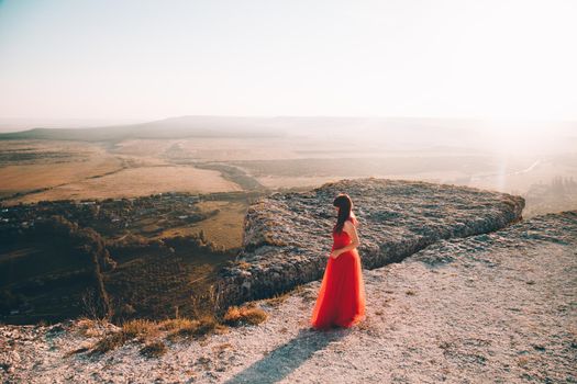 A girl in a red dress on the background of the mountains lifestyle. Illustrating articles about travel. A girl with a beautiful view. Vacation in Crimea. White rock. View of the villages. Lifestyle processing. Copy space .