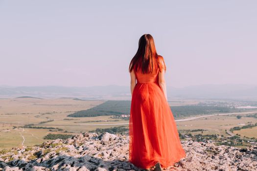 A girl in a red dress on the background of the mountains lifestyle. Illustrating articles about travel. A girl with a beautiful view. Vacation in Crimea. White rock. View of the villages. Lifestyle processing. Copy space .