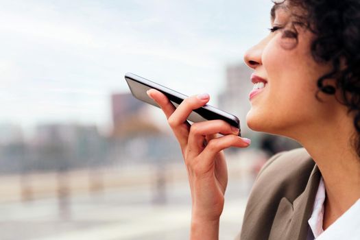 close up of a young woman smiling happy recording a voice message with a mobile phone, concept of communication and urban lifestyle, copy space for text
