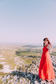 A girl in a red dress on the background of the mountains lifestyle. Illustrating articles about travel. A girl with a beautiful view. Vacation in Crimea. White rock. View of the villages. Lifestyle processing. Copy space .