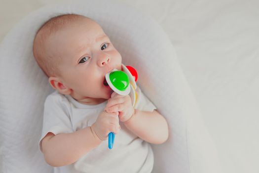 The kid is gnawing on a lifestyle rattle . Children's toys. An article about children. An article about children's toys. An article about teething. The rattle is colored. Copy Space