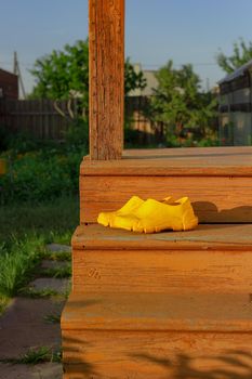 Yellow rubber muddy work shoes on old orange stairs on summer backyard at sunset, village and countryside authentic mood, vertical image