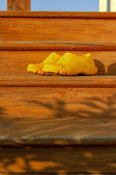 Yellow rubber muddy work shoes on old orange stairs on summer backyard at sunset, village and countryside authentic mood, vertical image