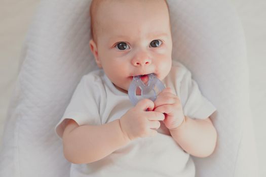 The kid is gnawing on a lifestyle rattle . Children's toys. An article about children. An article about children's toys. An article about teething. The rattle is colored. Copy Space