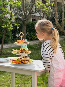 Little girl stands near a stand with fruits on the table. High quality photo