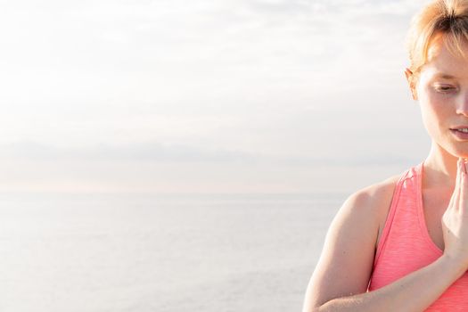 portrait of a blonde woman practicing yoga at dawn sitting in front of the sea, concept of mental health and relaxation, copy space for text