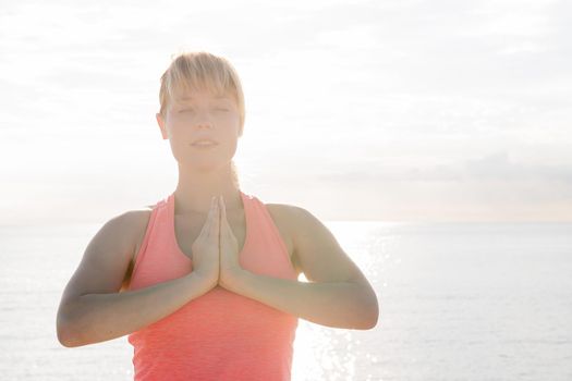 portrait of a blonde woman with her eyes closed practicing yoga at dawn in front of the sea, concept of mental health care and relaxation, copy space for text