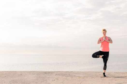 beautiful blonde woman practicing yoga balance at sunrise in front of the sea, concept of mental health and relaxation, copy space for text