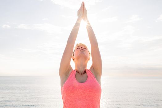 blonde woman meditating and practicing yoga at sunrise in front of the sea, concept of mental health care and relaxation, copy space for text