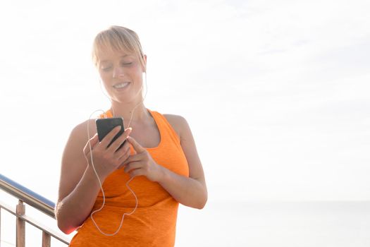 young sporty caucasian girl with earphones listening to music from her mobile phone, technology and healthy lifestyle concept, text copy space and lens flare effect