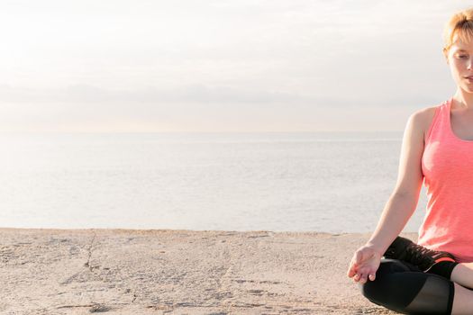 detail of a blonde woman practicing yoga in the lotus position at dawn sitting in front of the sea, concept of mental health and relaxation, copy space for text