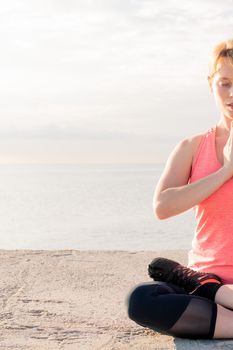 vertical photo of a blonde woman practicing yoga at dawn sitting in front of the sea, concept of mental health and relaxation, copy space for text