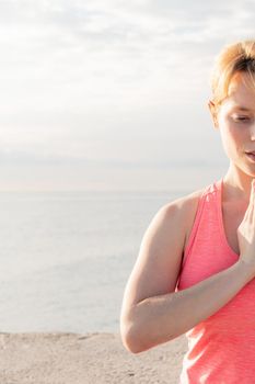 vertical portrait of a blonde woman practicing yoga at dawn sitting in front of the sea, concept of mental health and relaxation, copy space for text