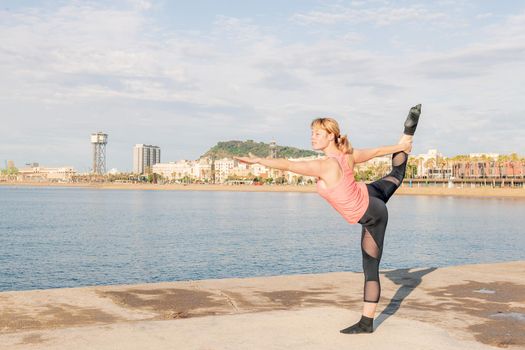 blonde sportswoman practicing balance and yoga stretches in front of the sea, concept of mental health and relaxation, copy space for text