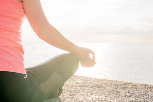 hand of an unrecognizable woman practicing yoga at dawn sitting in the lotus position in front of the sea, concept of mental health and relaxation, lens flare effect, copy space for text