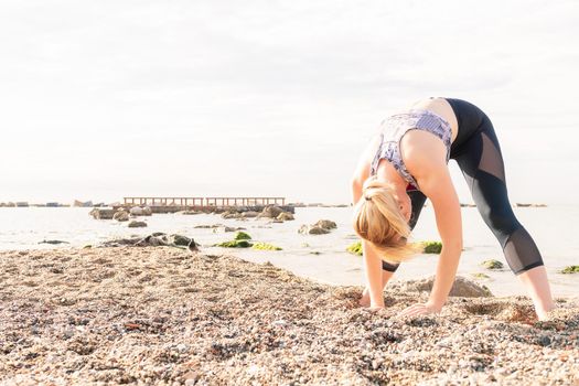 beautiful sporty blonde woman stretching out at dawn on the beach with her hands in the sand, healthy lifestyle and sports concept, text copy