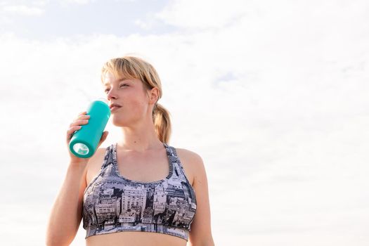 sportswoman with a bottle of water with the sky in the background, healthy lifestyle and sports concept, copy space for text
