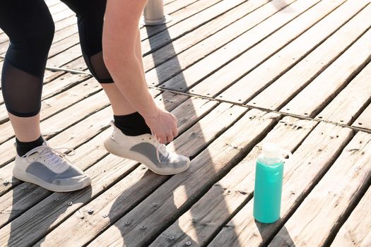 legs of an unrecognizable woman tying her running shoes next to her water bottle, concept of sport and healthy lifestyle, copy space for text