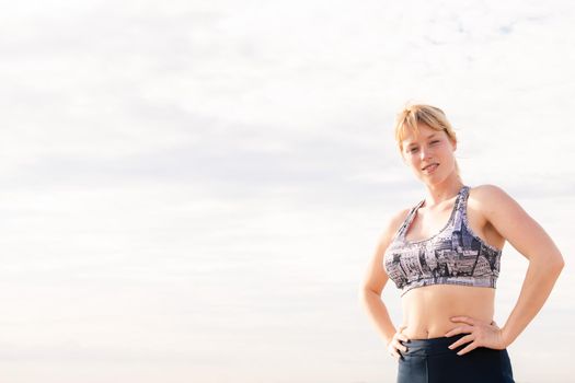 beautiful blonde sportswoman posing powerfully with her hands on her hips with the sky in the background, healthy lifestyle and sports concept, copy space for text