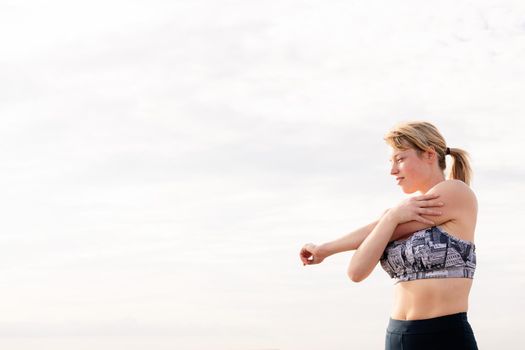 beautiful blonde sportswoman stretching with the sky in the background at dawn, healthy lifestyle and sports concept, copy space for text