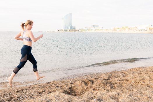 beautiful blonde sportswoman running along the beach in town, healthy lifestyle and sports concept, text copy