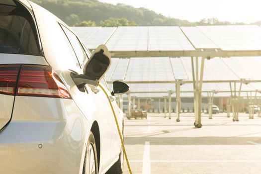 Charging electric car. Electric vehicles using renewable energy solar panels on green energy concept on modern city parking lot. Alternative energy for ecological cars under solar batteries