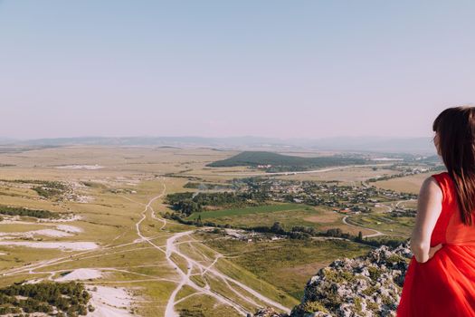 A girl in a red dress on the background of the mountains lifestyle. Illustrating articles about travel. A girl with a beautiful view. Vacation in Crimea. White rock. View of the villages. Lifestyle processing. Copy space .