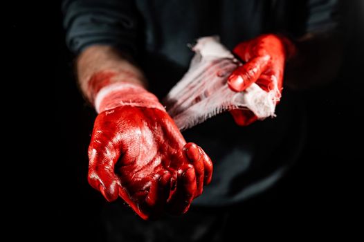 A man covered in blood bandages his hands