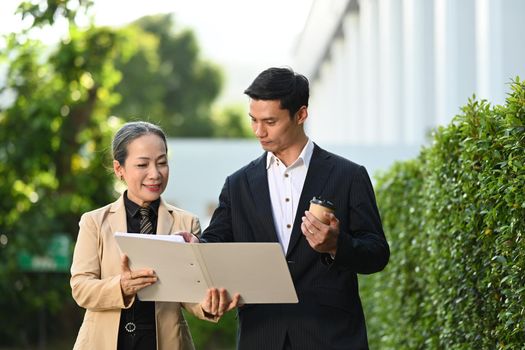 Two successful business people are discussing new project estate development, walking in modern office district.