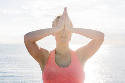 portrait of a blonde woman meditating and practicing yoga at dawn in front of the sea, concept of mental health care and relaxation