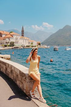 Summer photo shoot on the streets of Kotor, Montenegro. Beautiful girl in yellow dress and hat. smiling tourist girl with hat. Spectacular view of Montenegro with copy space. Ю fashion outdoor photo of beautiful sensual woman with blond hair in elegant dress and straw hat and bag, posing in Montenego's city Perast.