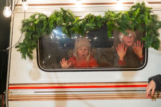 Two boys look out of the window of a Christmas-decorated camper
