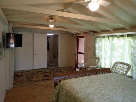 Inside Cottage Bedroom with Queen bed, Mounted HDTV, White Wicker chairs and bathroom.