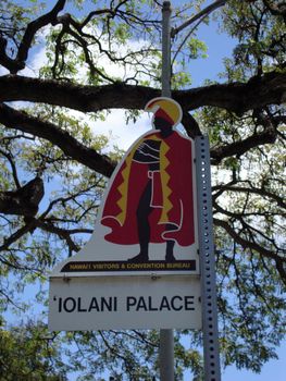 Iolani Palace Street Sign Marker on Oahu, Hawaii with tree branch, a blue sky with clouds. Iolani Palace is the only royal palace in the USA.