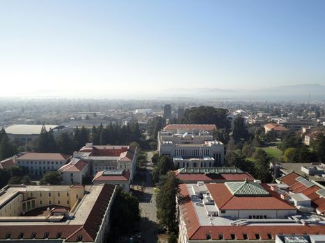 Birds eye view of Historic and modern Buildings of UC Berkeley Campus surrounded by trees with roads and paths intertwined with the landscape of the City of Berkeley in California looking towards San Francisco Bay on a very foggy day.  