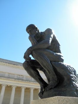 Side front profile of the masterpiece the Thinker by Rodin - The Thinker at the entrance of the Palace of the Legion of Honor in San Francisco with sunlight shinning down at it.      