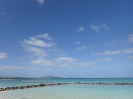 Pahonu Pond (Ancient Hawaiian Fishpond) with Shallow wavy ocean waters of Waimanalo bay looking into the pacific ocean with a blue sky full of clouds on Oahu.