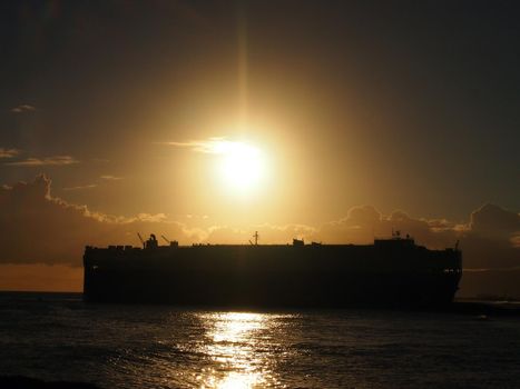 Dramatic Sunset over Pacific Ocean with Cargo Ship passing through the water off the coast of  Oahu, Hawaii.