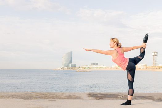 beautiful sportswoman practicing balance and yoga stretches at dawn in front of the sea, concept of mental health and relaxation, copy space for text