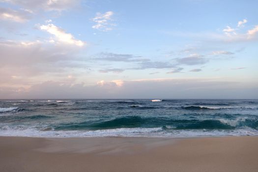 Waves break and crash towards the Hanakailio Beach with dramatic blue cloudy sky on the North Shore of Oahu, Hawaii. 