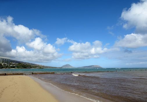 wall runs into the water at Kahala Beach with sparse clouds on a beautiful day on Oahu, Hawaii.   