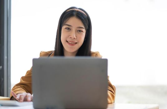 Charming Asian woman working at the office using a laptop Looking at the camera..