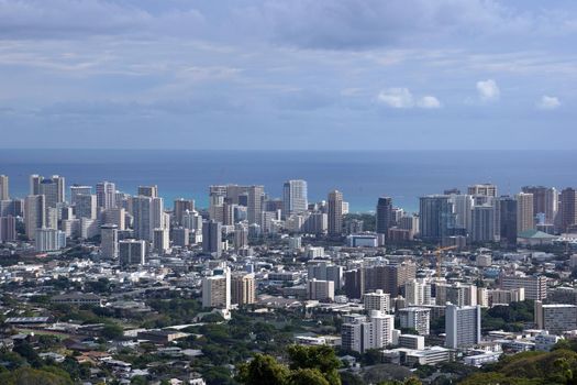 Honolulu cityscape, roads, buildings, skyscrapers, cranes, parks, and Pacific Ocean with clouds in the sky seen from up in the mountains on Oahu, Hawaii. 