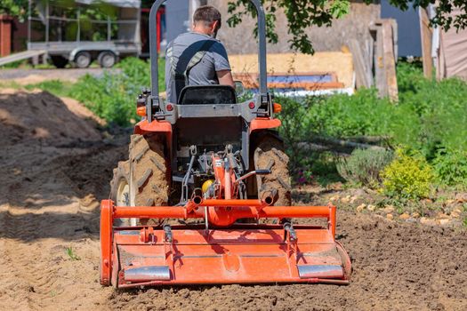 A man on a mini-excavator levels a piece of land, loosens the soil