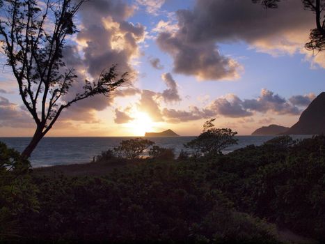 Early Morning Sunrise on Waimanalo Beach over Rabbit Island bursting through the clouds on Oahu, Hawaii with a path and vegetation leading the way to the ocean.