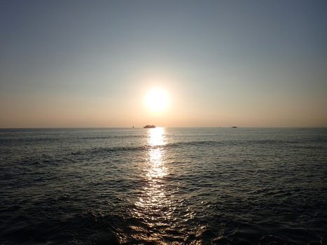 Sunset over the Pacific Ocean with light reflecting on water and boats moving on the horizon off the coast of Oahu, Hawaii.