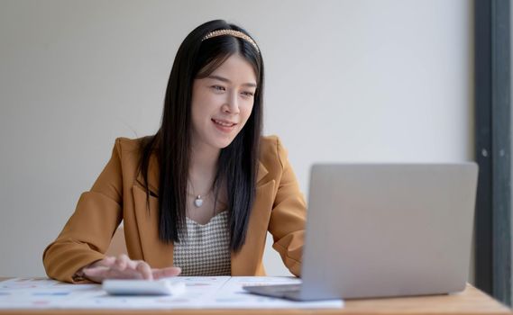 Charming asian businesswoman sitting working on laptop in office..