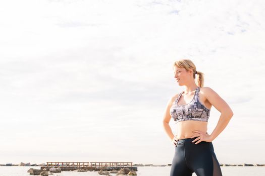 beautiful blonde sports woman posing powerfully on the beach with her hands on her hips, healthy lifestyle and sports concept, text copy