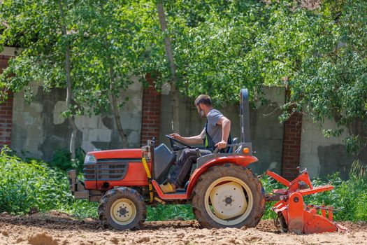A man on a mini-excavator levels a piece of land, loosens the soil