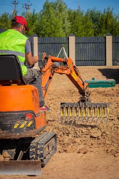A man on a mini-excavator levels a piece of land, loosens the soil